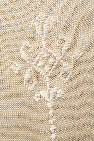 Detail of white embroidery on an off-white silk knit stocking.